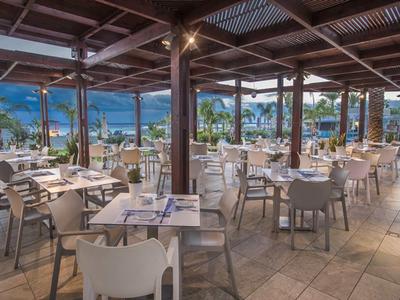 Otevřená restaurace s výhledem na moře a město s horami v pozadí.