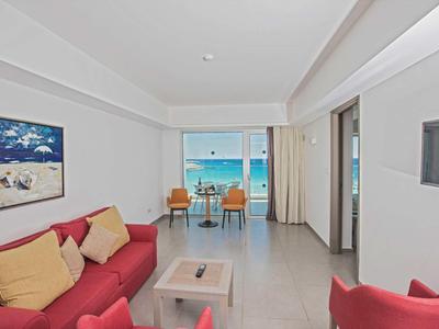 Světý hotelový pokoj s červenou pohovkou a výhledem na moře přes velká okna