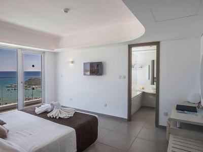 Moderní hotelový pokoj s výhledem na moře, manželskou postelí a přístupem do koupelny.