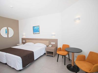 Hotelový pokoj s manželskou postelí, nočním stolkem, dvěma oranžovými křesly a malým kulatým stolkem.