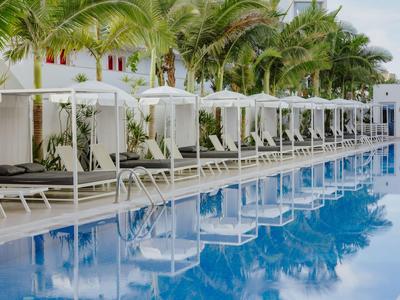 Moderner Pool mit weißen Liegen und Palmen in einem Hotelresort.