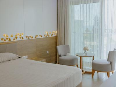Modernes Hotelzimmer mit Doppelbett, zwei Sesseln und Balkon mit Sicht nach draußen.
