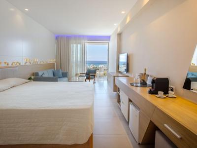 Modernes Hotelzimmer mit großem Bett, schlichter Einrichtung und Balkon mit Meerblick.