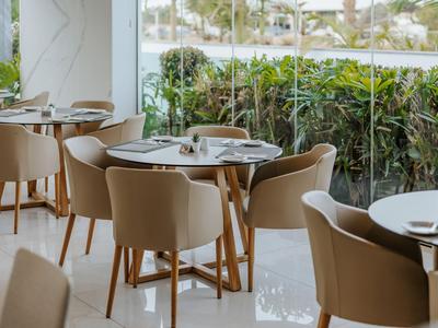 Moderner Hotelrestaurantbereich mit runden Holztischen und beigen Polsterstühlen neben großen Fenstern.