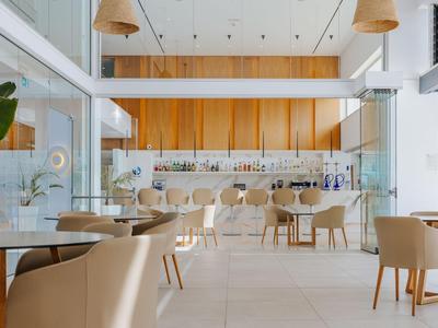 Moderner Hotel-Loungebereich mit beige Polstersesseln, Holzakzenten und Tageslicht.