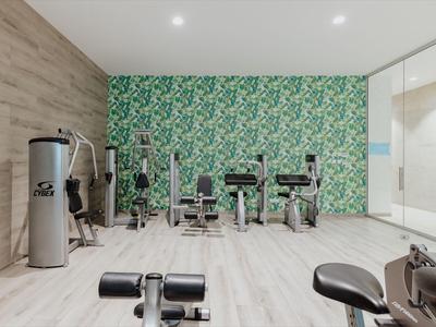 Moderner Fitnessraum mit Geräten vor einer grünen Wand und Holzfußboden in einem Hotel.