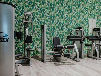 Fitnessraum mit modernen Geräten und grüner Blättertapete, ideal für Hotelgäste.