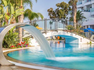 Moderner Pool mit Wasserfall, Brücke, Palmen und blauer Sonne an einem sonnigen Tag.