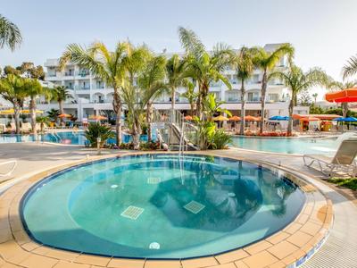 Vasca idromassaggio rotonda all'aperto circondata da palme e lettini davanti a un edificio dell'hotel.