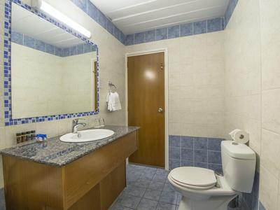 Kleines Badezimmer mit Waschbecken, Spiegel, Toilette und brauner Holztür. Wände weiß-blau gefliest.