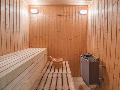 Holzsauna mit Bänken, Holzeimer, Kelle und elektrischem Saunaofen an der rechten Wand.