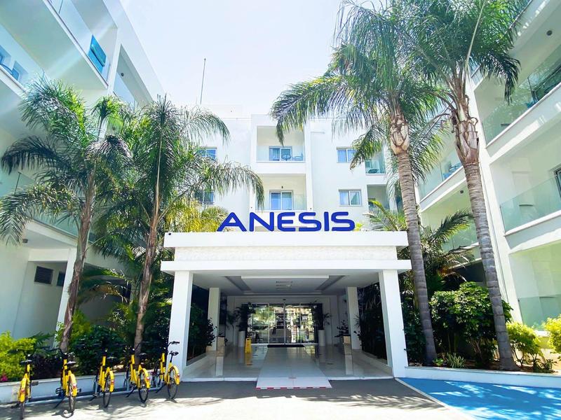 Modernes, weißes Gebäude mit Palmen und gelben Fahrrädern vor dem Eingang "ANESIS".