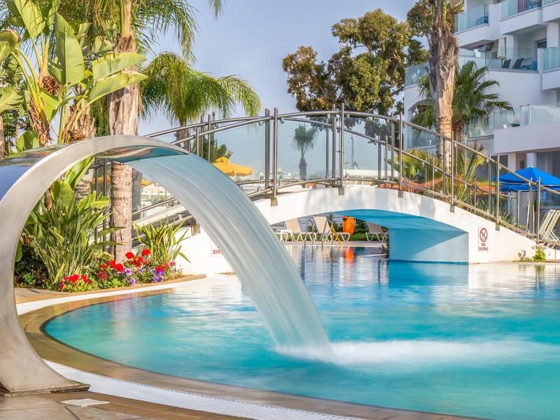 Moderner Pool mit Wasserfall, Brücke, Palmen und blauer Sonne an einem sonnigen Tag.
