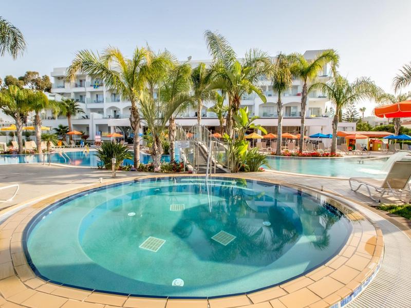 Runder Whirlpool mit klarem Wasser vor Palmen und Hotelgebäuden bei sonnigem Wetter.