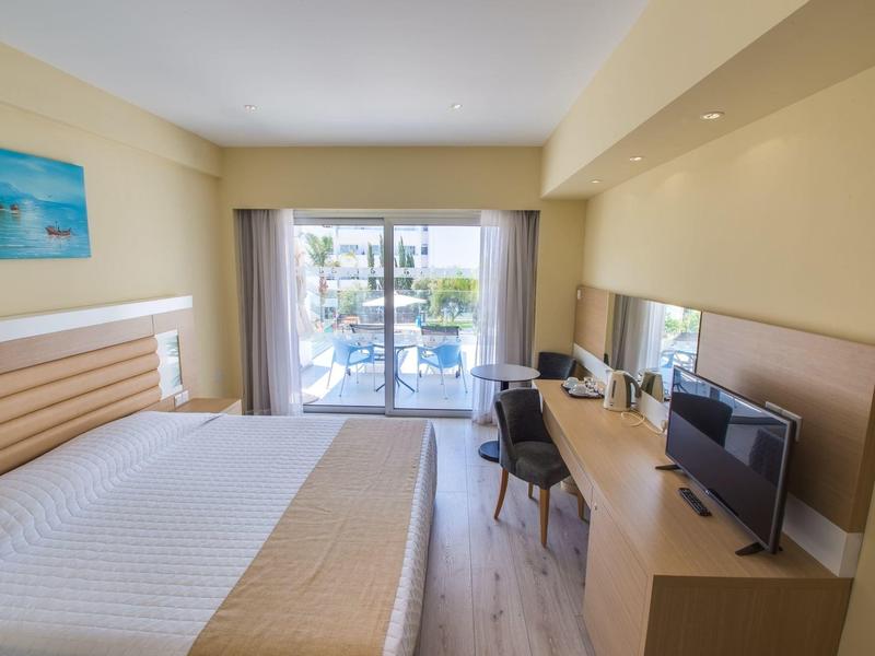 Modernes Hotelzimmer mit großem Bett, Schreibtisch, Fernseher und Balkon mit Gartenblick.