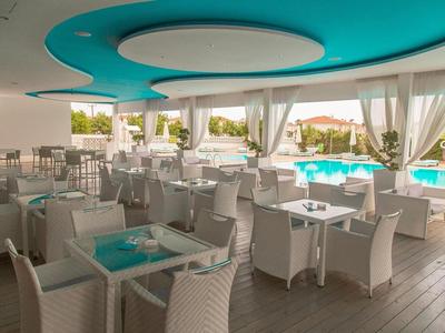 Moderner Außenbereich eines Hotels mit weißen Stühlen, Tischen und Blick auf einen Pool.