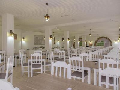 Großer, heller Speisesaal mit vielen weißen Stühlen und Holztischen im Hotel.