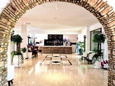 Ein Empfangsbereich mit einem steinernen Bogen, hellen Fliesen und Empfangstresen im Hintergrund.