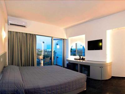 Modernes Hotelzimmer mit großem Bett, Fernseher und Blick auf Stadt bei Sonnenuntergang