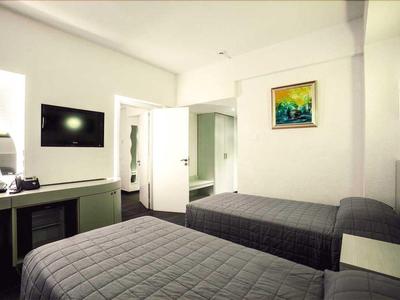 Helles Hotelzimmer mit zwei Einzelbetten, TV und geöffnetem Badezimmer.