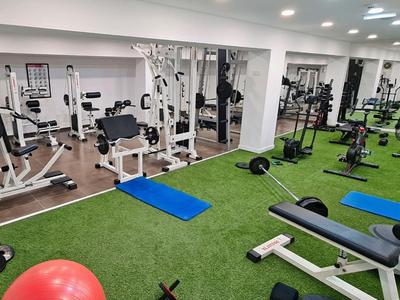 Fitnessraum mit verschiedenen Trainingsgeräten und grünem Kunstrasenboden.