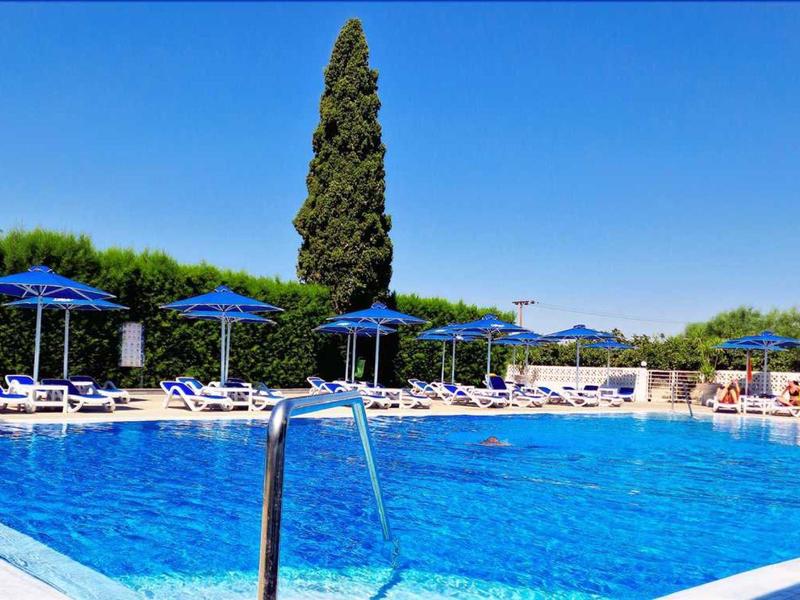 Großer blauer Pool mit weißen Liegestühlen und blauen Sonnenschirmen unter klarem Himmel.