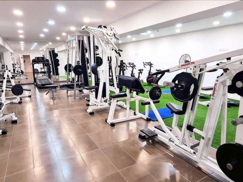 Modernes Fitnessstudio mit zahlreichen weißen Trainingsgeräten und Holzfußboden, gut beleuchtet.