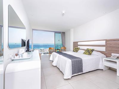 Světý hotelový pokoj s manželskou postelí, balkonem a výhledem na moře za dne.