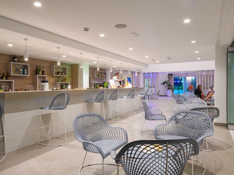 Moderner Hotelbarbereich mit weißen Möbeln und entspannter Atmosphäre bei gedämpftem Licht.