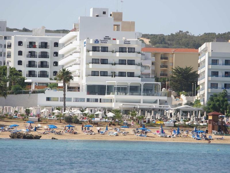 Strand mit Sonnenliegen und Palmen vor mehrstöckigen Hotels am Meer.