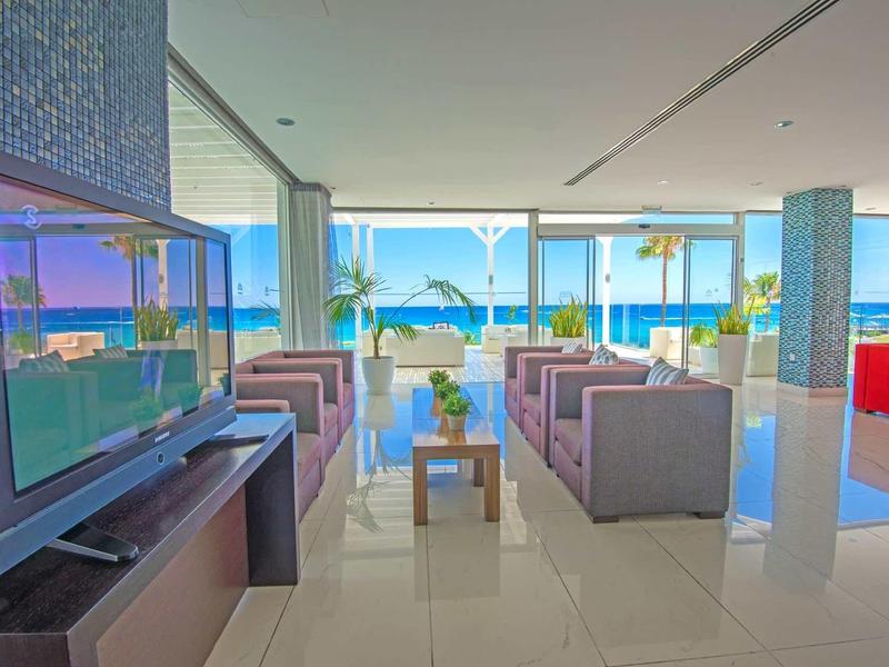 Moderne Lobby mit großen Fenstern, Polstermöbeln, TV und Meerblick bei klarem Wetter.