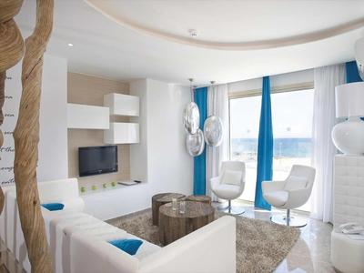 Modernes Hotelzimmer mit weißen und blauen Akzenten, Sitzbereich und großen Fensterfronten.