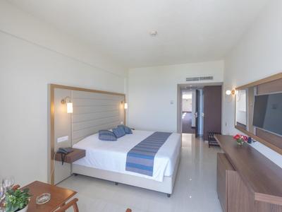 Hell eingerichtetes Hotelzimmer mit Doppelbett, Fernseher an der Wand und modernem Mobiliar.