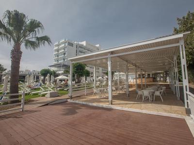 Relax zóna s krytou terasou, stoly a výhledem na palmy a lehátka v hotelové zahradě.