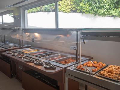 Großes Buffet mit warmen Speisen in Edelstahlbehältern und Beleuchtung darüber.