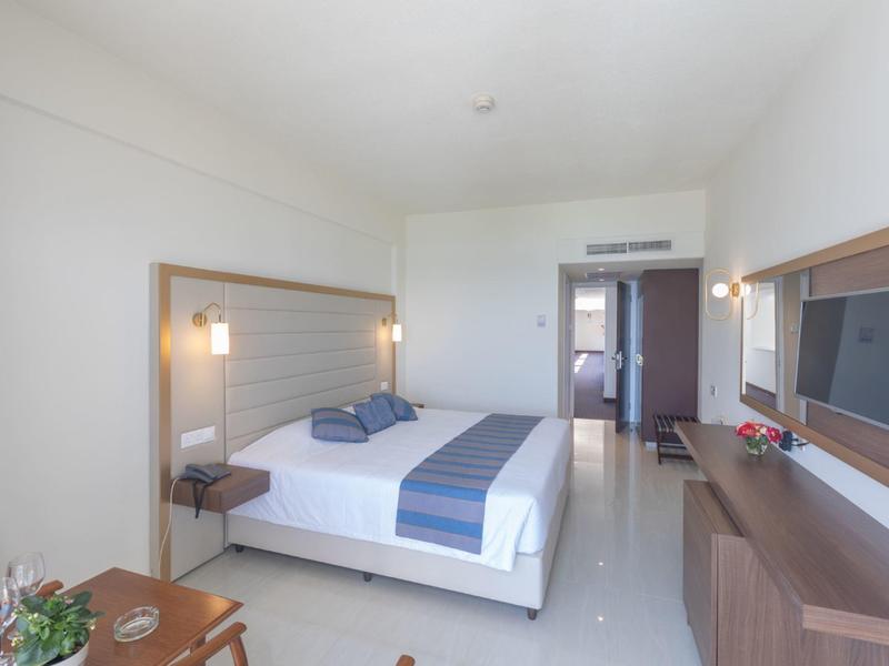 Hell eingerichtetes Hotelzimmer mit Doppelbett, Fernseher an der Wand und modernem Mobiliar.