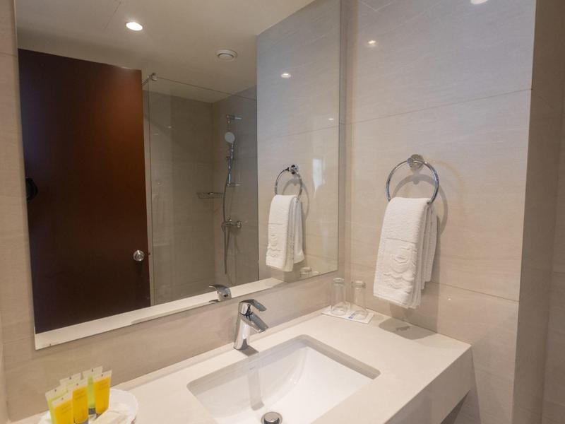 Helles Badezimmer mit großem Spiegel, weißem Waschbecken, Handtüchern und Duschkabine im Hintergrund.