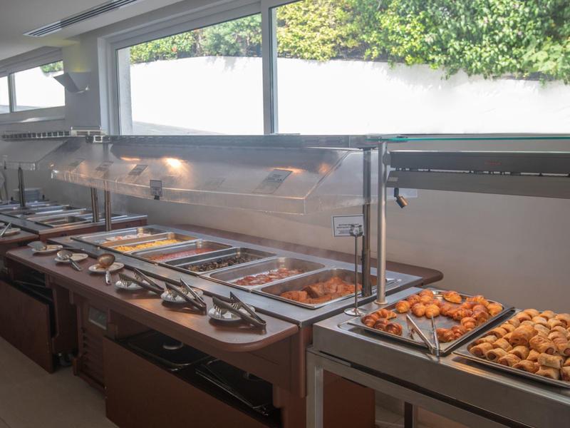 Großes Buffet mit warmen Speisen in Edelstahlbehältern und Beleuchtung darüber.