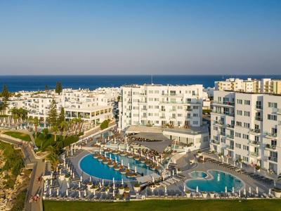 Moderner Hotelkomplex mit Pools, Liegen und Blick auf das blaue Meer unter klarem Himmel.