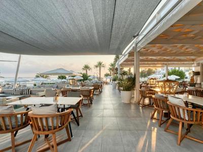 Ristorante all'aperto con tavoli e sedie, vista mare e palme al tramonto.