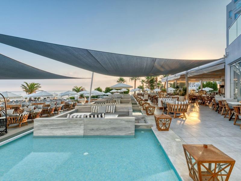 Espace extérieur moderne avec piscine, sièges et voiles d'ombrage, vue sur la mer en arrière-plan.