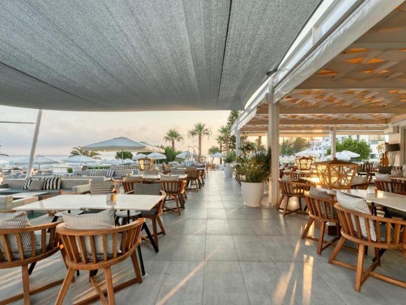 Terrasse extérieure moderne de restaurant avec tables en bois et vue sur la mer au coucher du soleil.