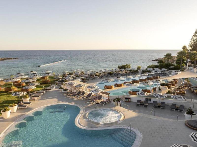 Piscine d'hôtel de luxe avec vue sur la mer, de nombreuses chaises longues et parasols.