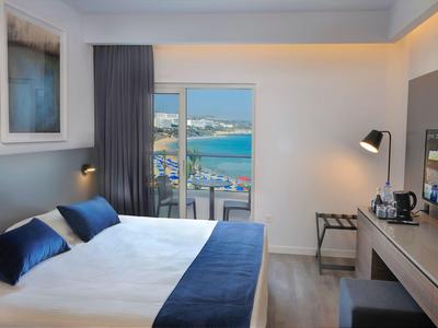 Modernes Hotelzimmer mit großem Bett, Schreibtisch und Blick auf Meer und Stadt.