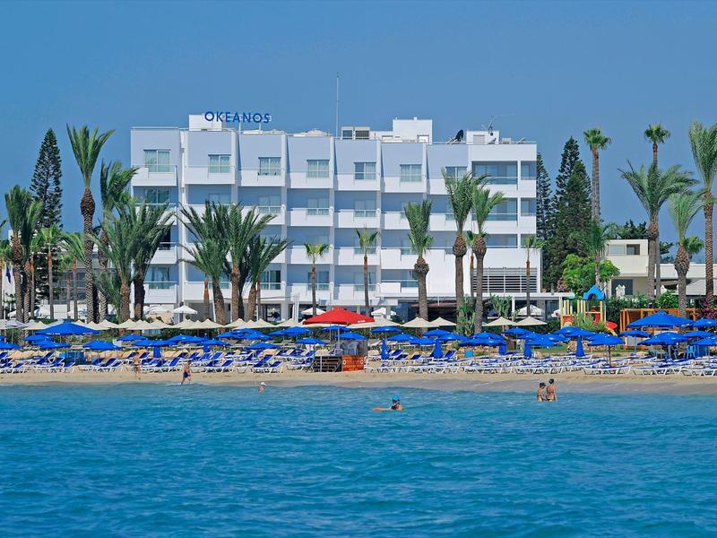 Modernes Hotel an einem Sandstrand mit Sonnenschirmen und Palmen am Meer