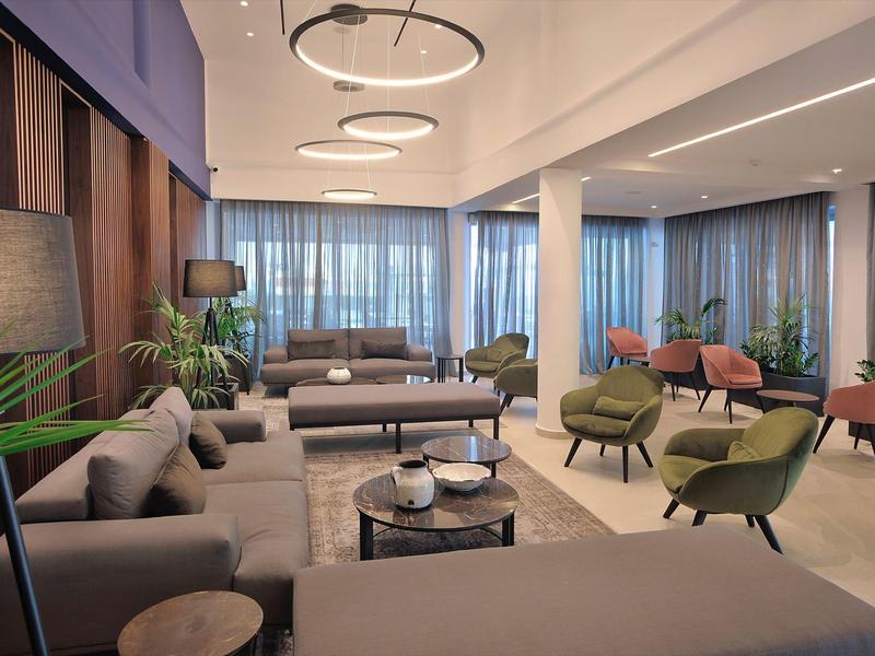 Moderner Hotel-Loungebereich mit Sesseln, Sofas, Pflanzen und großen Fenstern mit Vorhängen.