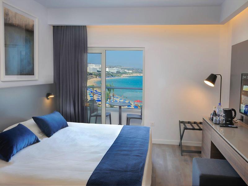 Helles Hotelzimmer mit Doppelbett, Balkon und Meerblick bei Tageslicht.