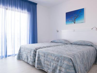 Hell eingerichtetes Hotelzimmer mit zwei Einzelbetten und blauen Vorhängen am Fenster.