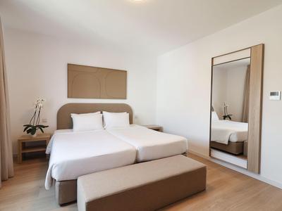 Helles Hotelzimmer mit zwei Einzelbetten, großem Spiegel und minimaler Dekoration.