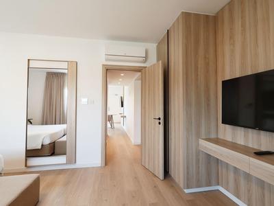 Moderner Hotelraum mit Holzvertäfelung, kleinem Fernseher und Blick in einen hellen Flur.